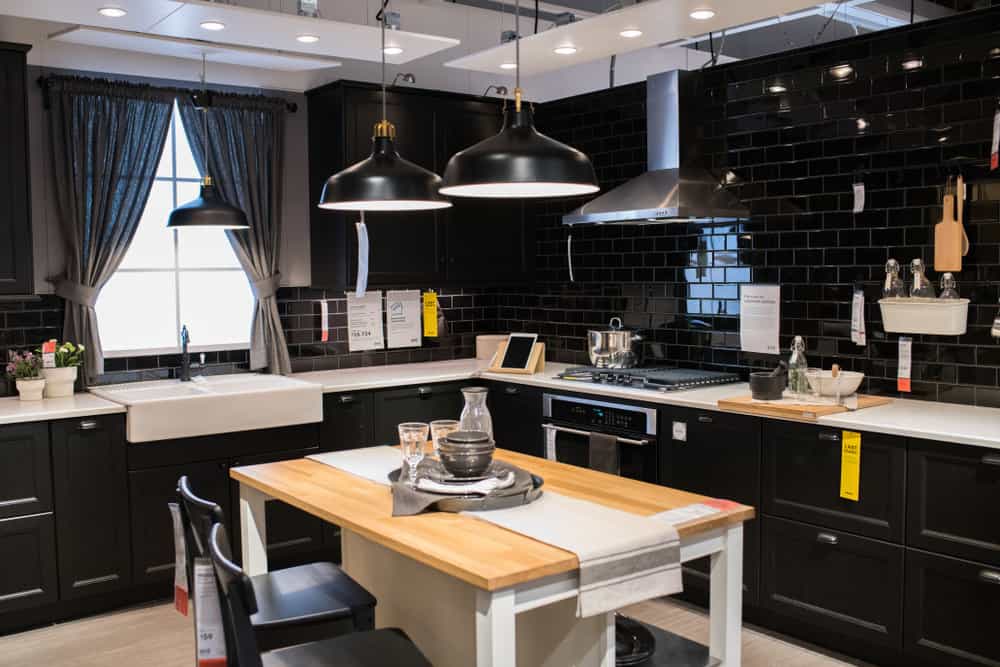 这个超级优雅的厨房有黑色的墙壁，黑色的橱柜和黑色的吊灯。浅色的地板、台面和金色的木桌与厨房的黑色饰面形成鲜明而美丽的对比。这个厨房受到亚洲主题的影响。