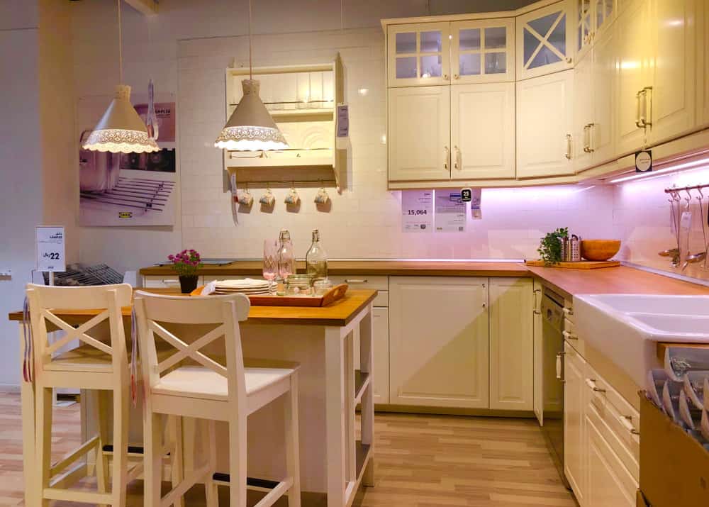 这个美丽的乡村风格的厨房配有金色调的地板和两个漂亮的蕾丝灯。橱柜下面的粉色灯光为房间增添了玫瑰色的色调，桌子上的小瓶红玫瑰使这个厨房成为浪漫晚餐的完美场所。