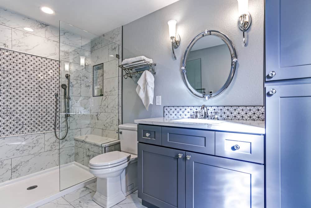 这个漂亮的浴室并没有那么大，但镜子和玻璃的巧妙使用使它看起来更宽敞。白色和灰色的大理石墙壁和地板，白色的固定装置和圆形的镜子，还有两盏灯，让这个房间看起来像被包裹在一个泡泡里。