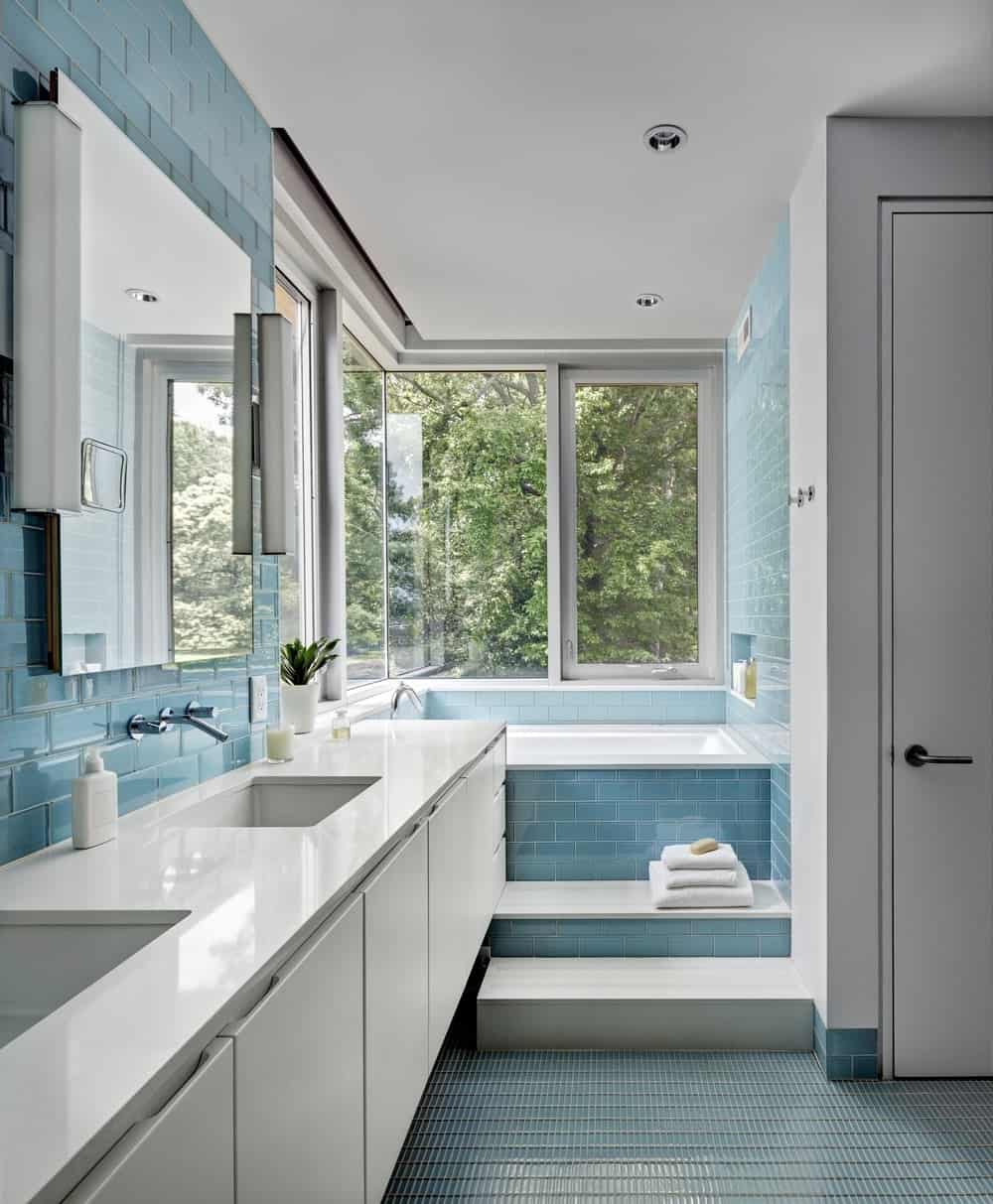 这个浴室有蓝色瓷砖的台阶和下沉的浴缸，给人一种游泳池的错觉。浴缸旁边的窗户可以看到外面的美景，使这个浴室成为一个放松的温泉般的下午的完美场所。