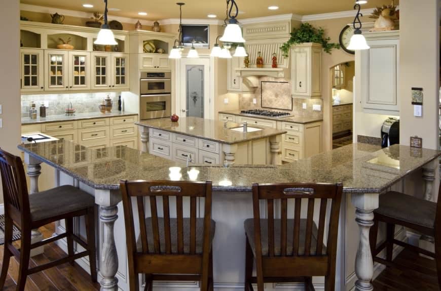 这间家庭风格的厨房有一个几何形状的大岛台，顶部是宽大的大理石，还有一个较小的岛台，里面有抽屉和橱柜，可以存放物品。头顶水仙花灯的明亮照明，厨房以石头和奶油为主题，给人一种家的感觉。
