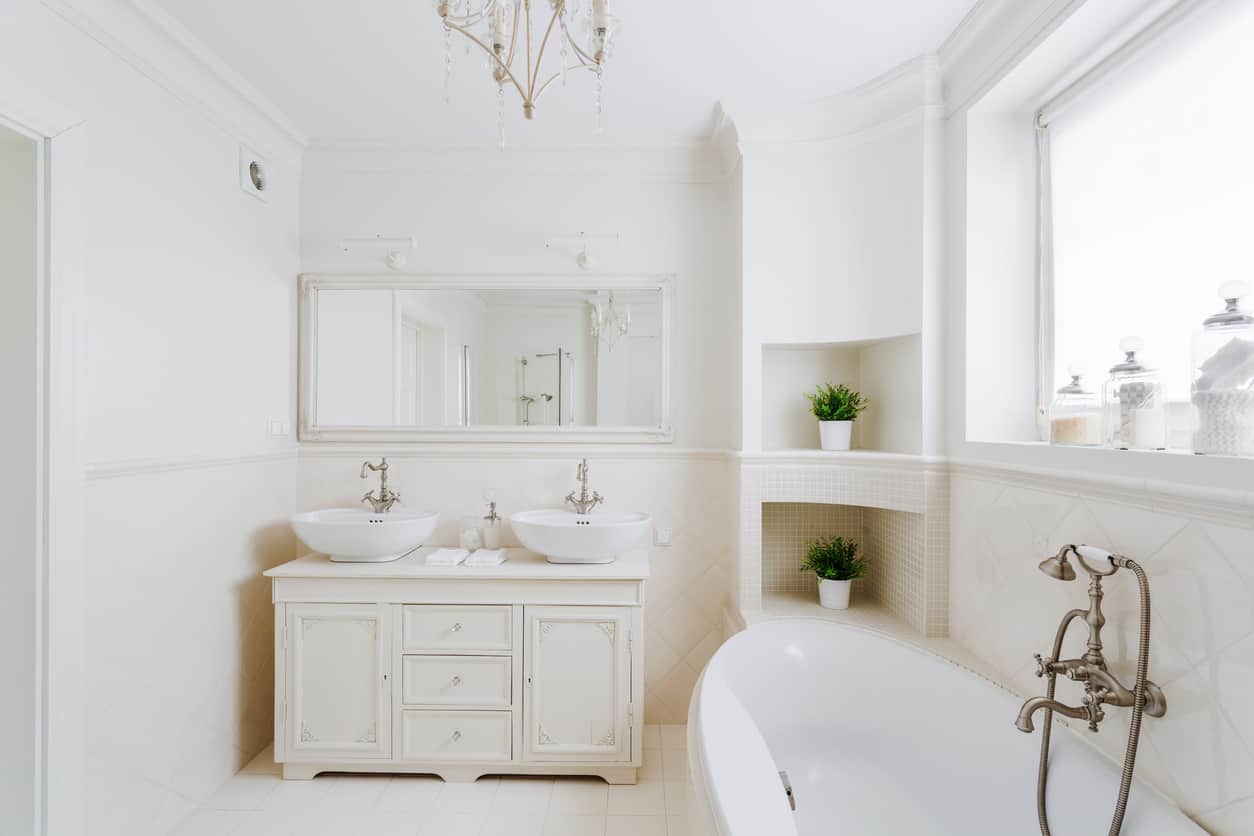 这个白色瓷砖的主浴室围绕着一扇大墙跨窗而建，带有纯白复古风格的梳妆台，双碗水槽和刷过的复古铜色装置给人一种优雅的感觉。白色皇冠造型和一个大的椭圆形部分独立式花园浴缸，为您带来轻松的沐浴体验。