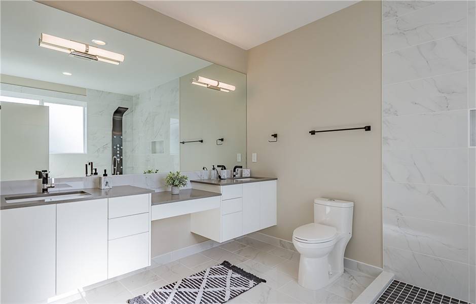 这间主浴室设有一个浮动的双水槽梳妆台和一个光滑的淋浴区，反射在巨大的镜子中。大理石瓷砖墙和后挡板为房间增添了优雅的触感。