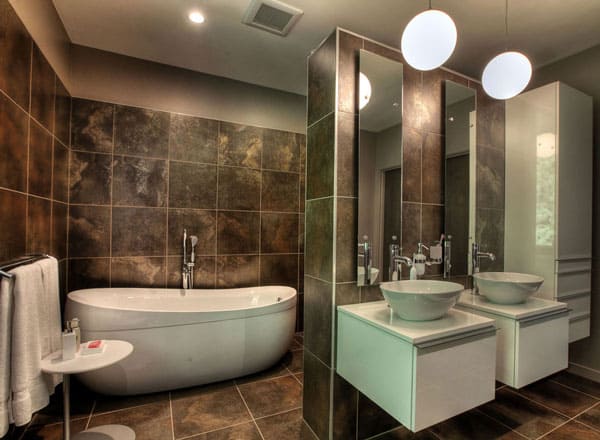 这间主浴室的地砖采用了深色大理石色调，一直延伸到墙壁上。这使得白色的独立式浴缸和浮动水槽脱颖而出。