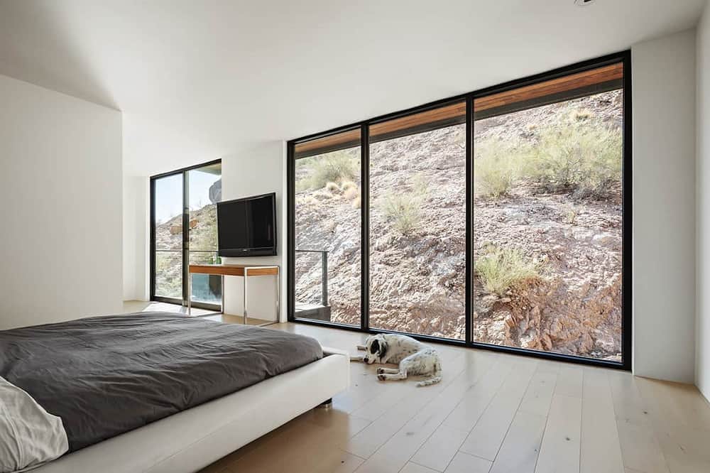 这是现代和极简主义卧室的全貌，硬木地板中间有一张白色的床，被玻璃墙照亮。