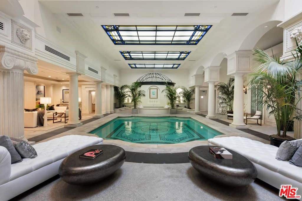 这个宏伟的室内游泳池是宏伟和奢华的。它就在房子的正中央，两边有高大优雅的白色柱子，两端有放松的椅子，游泳池周围有一些新鲜的绿色花盆。