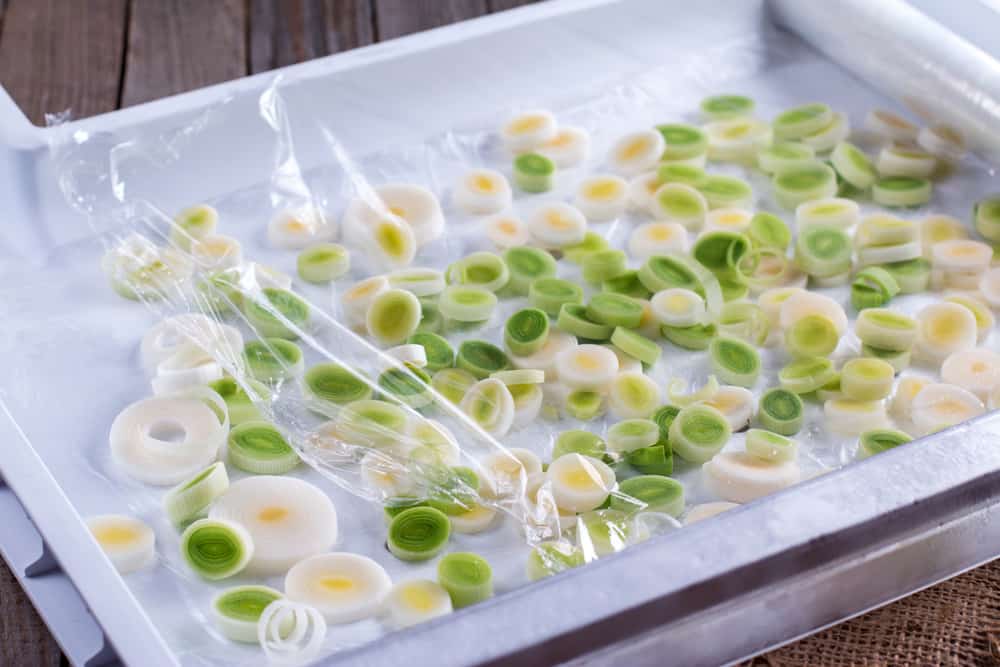 切碎的韭菜放在白色泡沫塑料托盘上，上面盖上保鲜膜