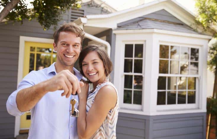 妻子和丈夫微笑着拿着钥匙站在他们的新家门前