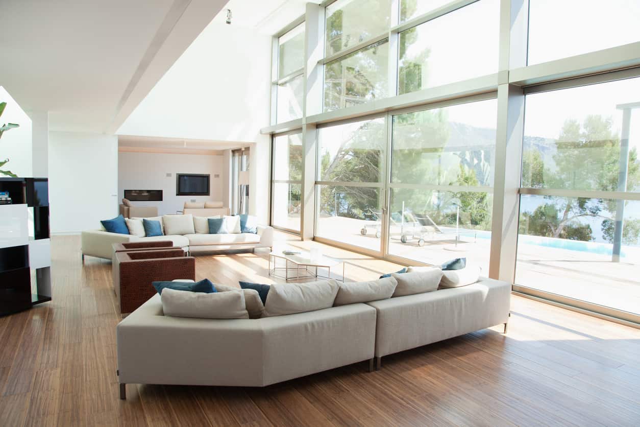 一间宽敞的现代客厅，有落地窗和中性色调的硬木地板，并配有蓝色的靠垫。