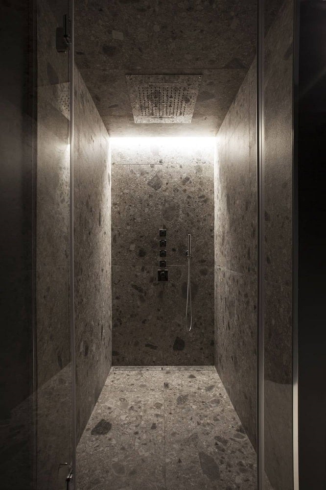 这是对现代浴室的近距离观察，展示了步入式淋浴区，墙壁、地板和天花板上一致的灰色调，辅以淋浴装置和玻璃门。