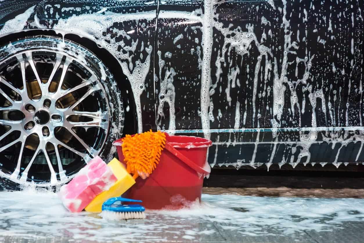 不同类型的洗车工具和后面的湿肥皂黑汽车。