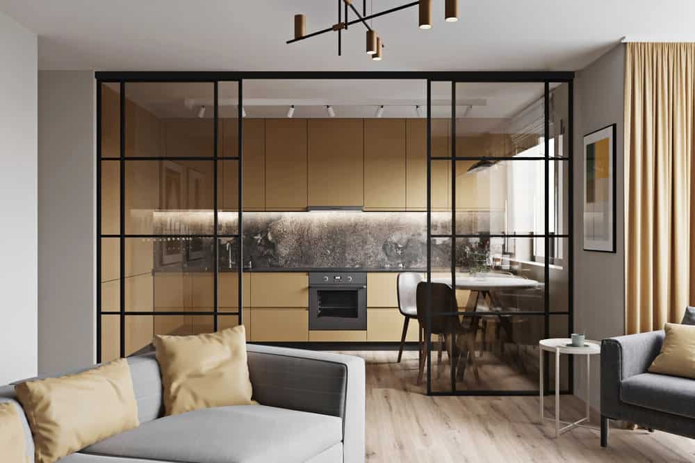 这是一个近距离观察公寓客厅的灰色沙发和厨房和餐厅的有一个清晰的视图通过一组玻璃墙壁滑开。