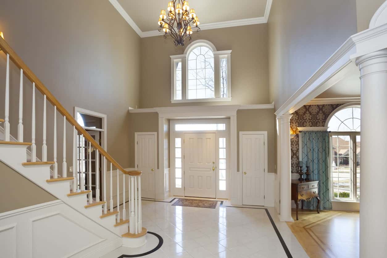 这个优雅的白色门厅设有瓷砖地板和由优雅的吊灯照亮的美丽楼梯。