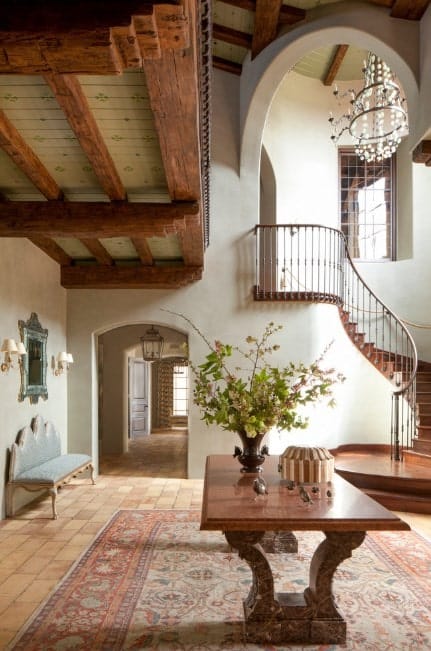 这个门厅以瓷砖地板为特色，上面有一个优雅的地毯。正上方是一张中间的桌子。一盏漂亮的枝形吊灯照亮了楼梯。