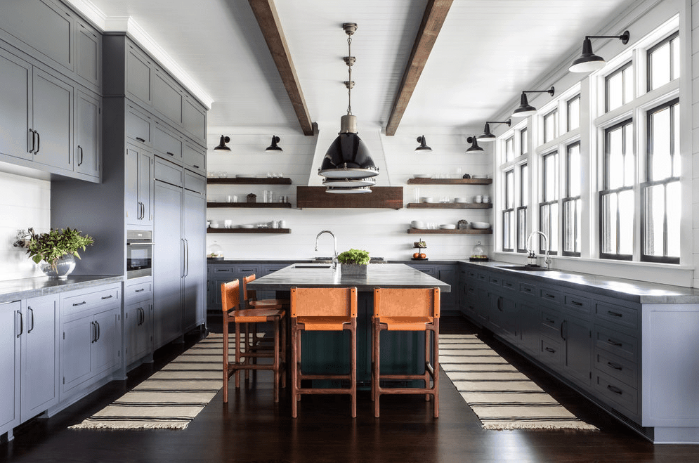 宽敞的农舍厨房配有蓝色橱柜，白色天花板上的木梁和chango & co设计的质朴的开放式浮动货架。