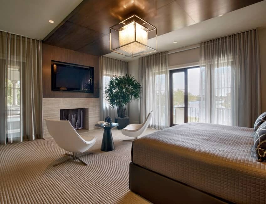 这间主卧室从天花板到地毯地板都包裹着温暖的色调，营造出亲密舒适的氛围。透明的窗帘和有质感的床上用品和地毯地板增加了视觉趣味，而现代特色椅子的清新白色与之形成鲜明对比。