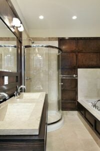 深色木橱柜使这间主浴室与众不同，设有一个浸泡浴缸和一个玻璃封闭的步入式淋浴间。木制梳妆台里有两个大理石水槽，梳妆台上方有一面大镜子和壁挂式灯具。