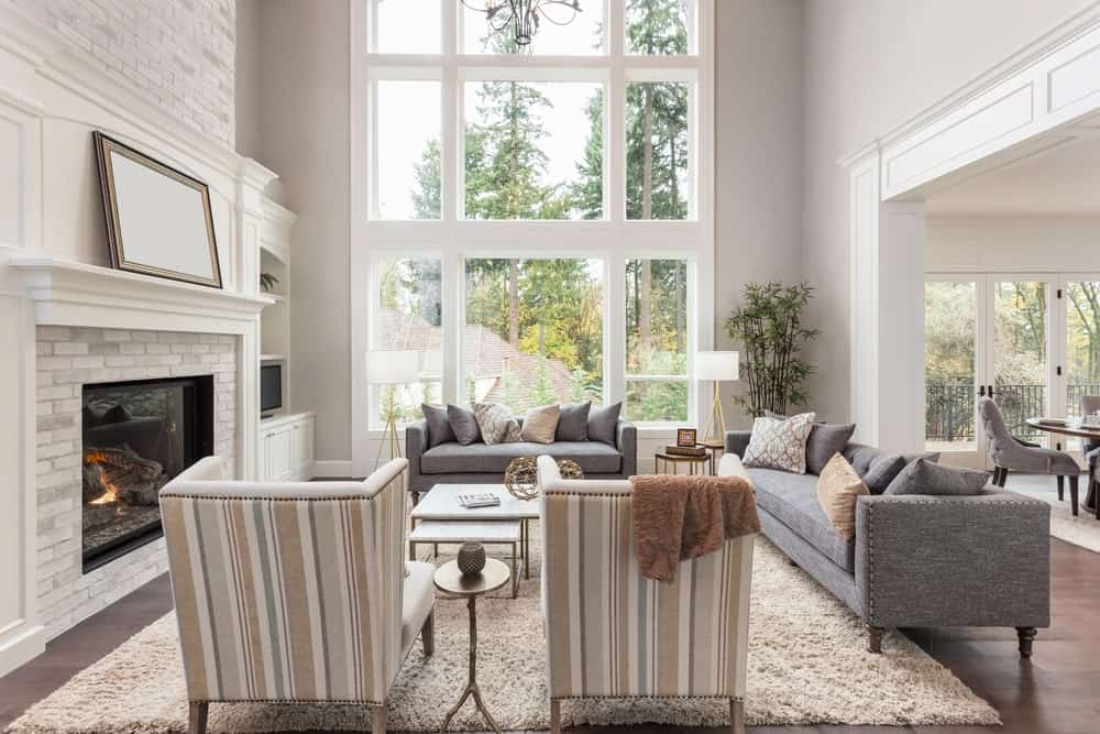宽敞的客厅，白色地毯上有灰色沙发和优雅的座椅。壁炉使温度保持温暖。高高的天花板使这个房间看起来美极了。