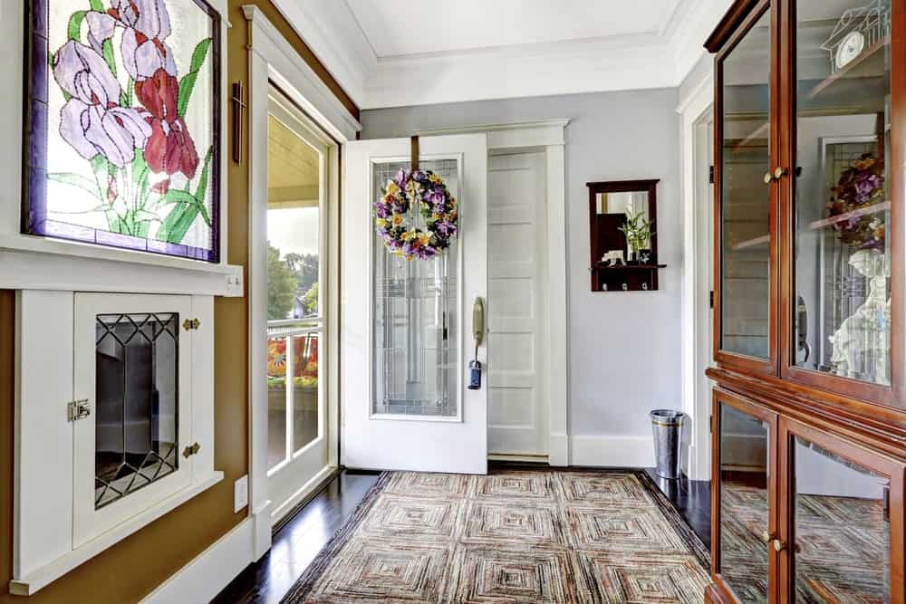这个简单而温馨的工匠风格的门厅展示了主要的木结构，使这个门厅具有独特的外观，如木门，天花板和深棕色的木制橱柜，用于装饰玻璃面板。对面是一扇明亮的彩色玻璃窗。