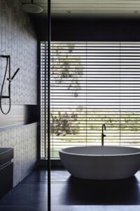 如果真的有亚洲风格的室内设计，那么这就是它。深色的材料，自然的照明和极简的线条创造了一个主浴室，设有一个独立的浴缸，设置在浓缩咖啡色的地板上。