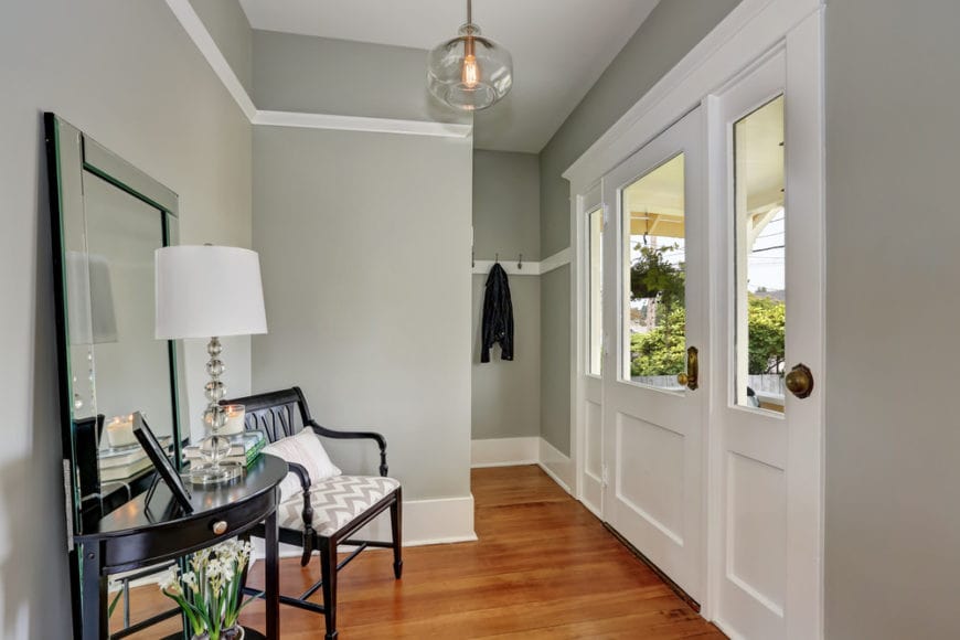 小而紧凑的门厅有灰色的墙壁，使深色的木质元素脱颖而出，就像装饰着一面大镜子的扶手椅和控制台桌子。这些都有一个简单的玻璃球形吊灯挂在白色天花板上。