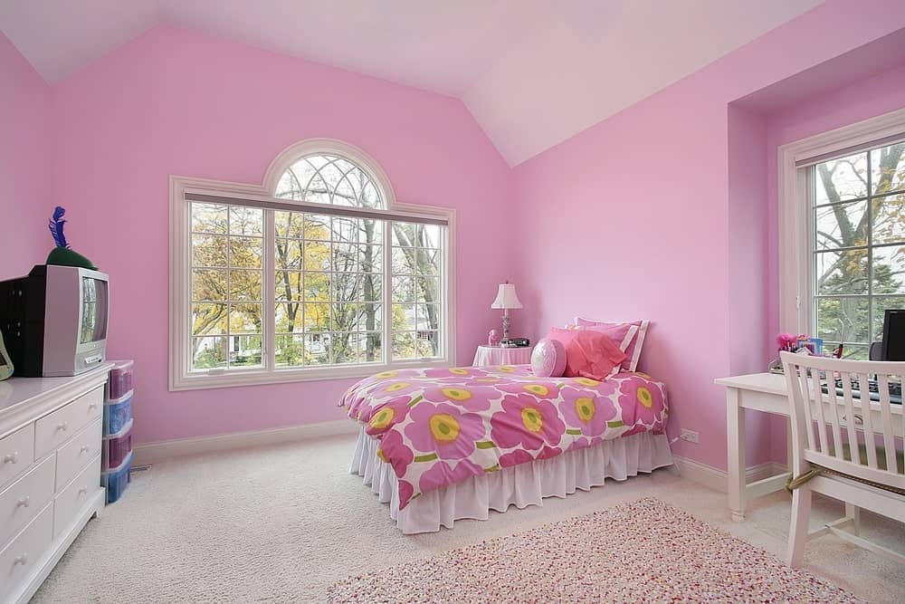 大女孩的卧室被粉红色的墙包围着。地毯地板看起来很适合这个房间。还有一张书桌，放在窗边。