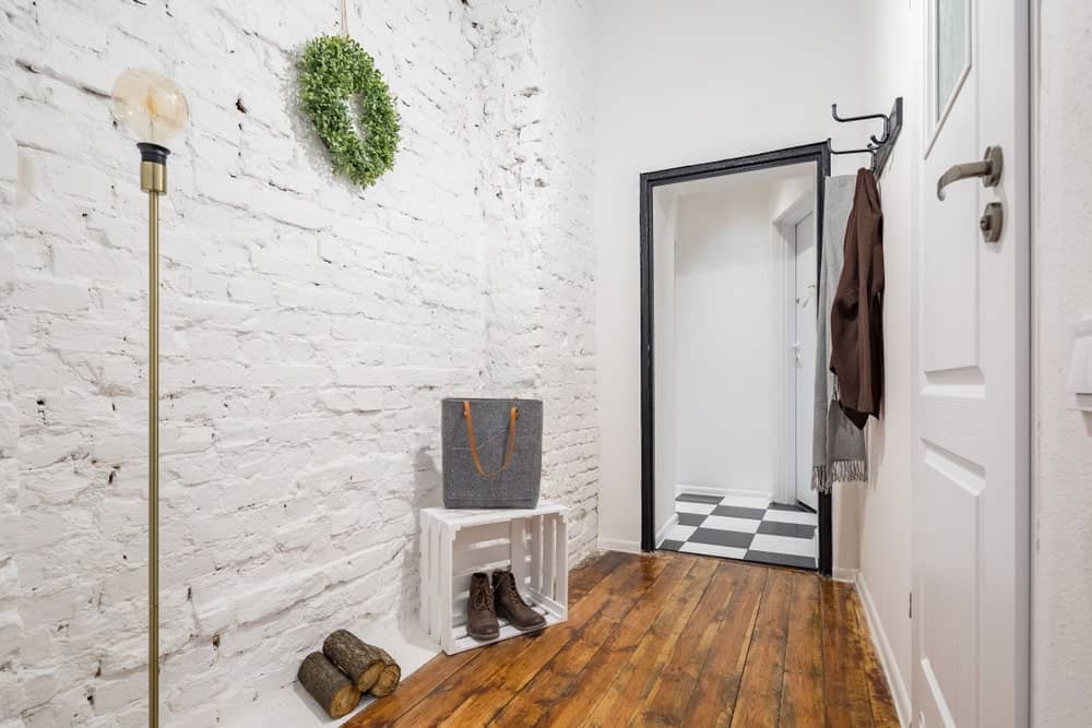 这个小Industrial-style门厅白色纹理砖墙,辅以转换到一个黑色的硬木地板和白色花纹地板在跨越的门槛的入口通道。