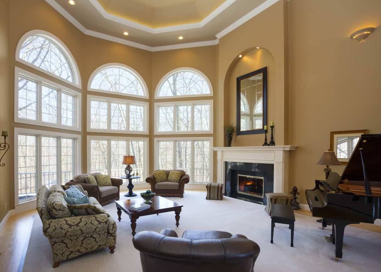 一个优雅的正式客厅，有高高的天花板和覆盖硬木地板的巨大地毯。该房间还设有一座壁炉和一架漂亮的钢琴。