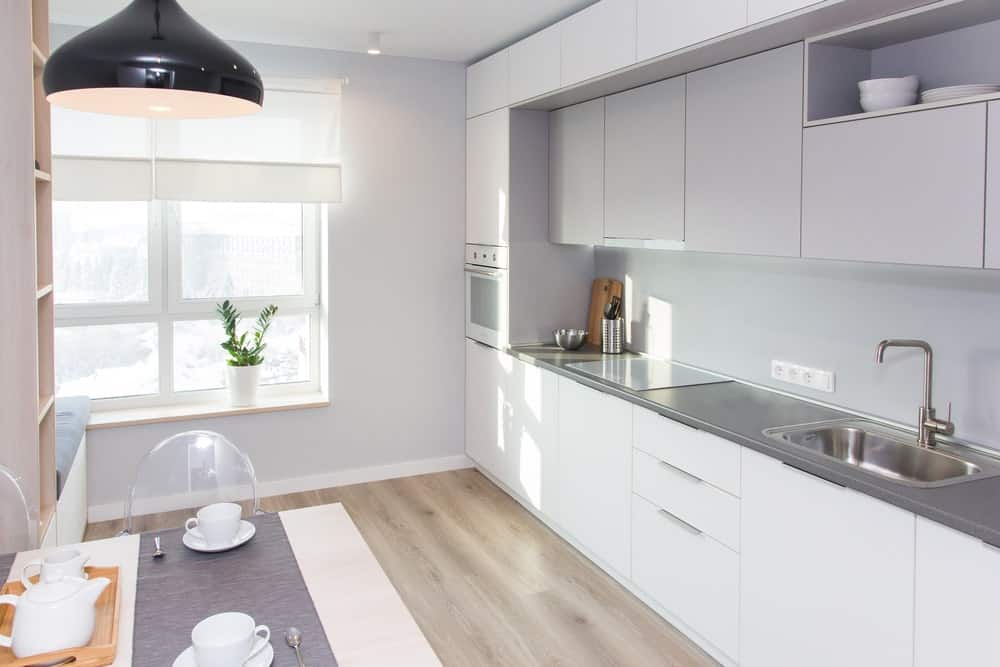 这间斯堪的纳维亚风格的厨房设有硬木地板、白色橱柜和柜台，中间设有餐桌。