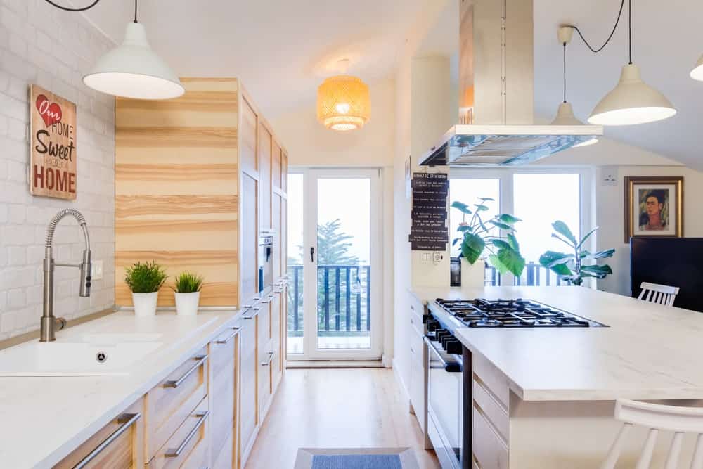 这个斯堪的纳维亚风格的厨房拥有白色台面和木制橱柜和厨房柜台的组合。温暖的白色吊灯看起来与厨房的风格完美搭配。