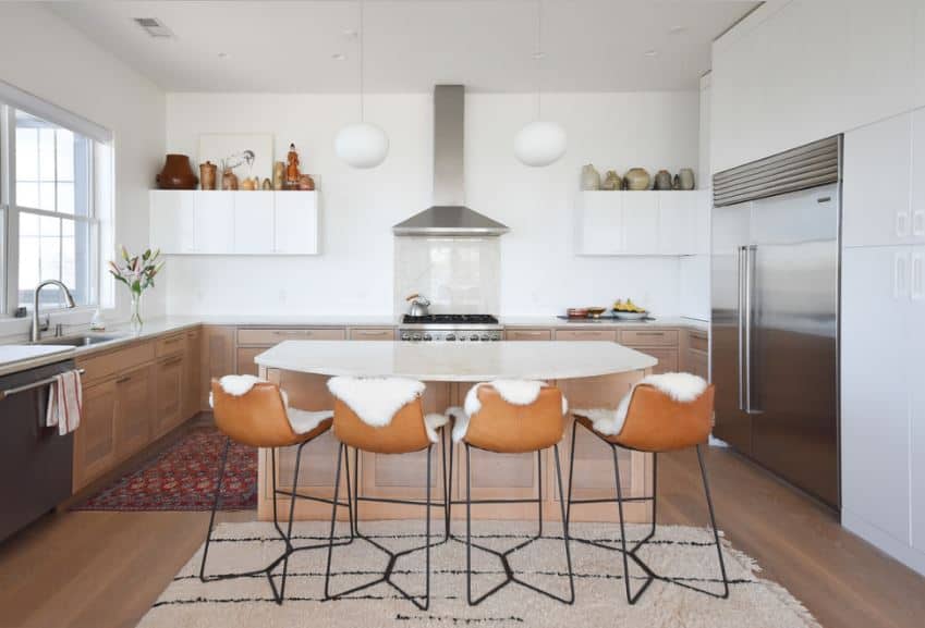 现代厨房岛面临的凳子是缓冲与白色皮草配白色的厨房的台面和墙壁。烹饪区两侧是两个球形吊坠灯挂在白色的天花板。