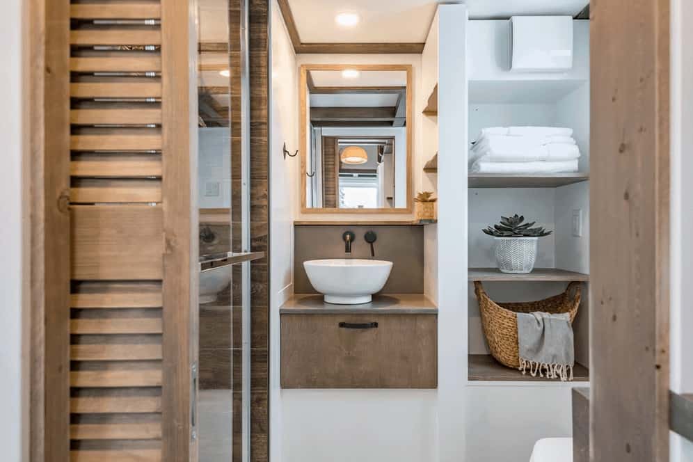 带玻璃淋浴的小房子浴室，带现代水龙头的容器水槽，天花板上的木饰和时尚的内置架子。