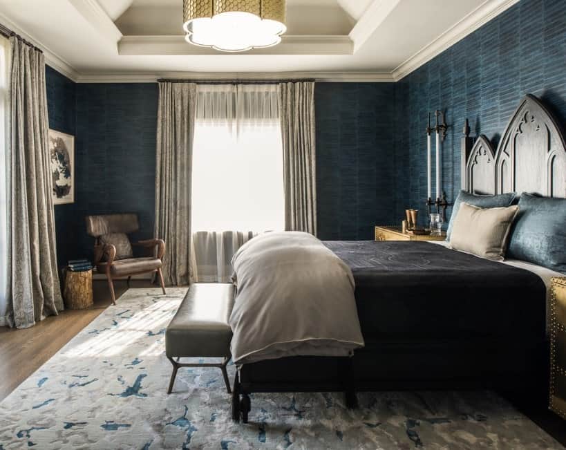 一个优雅的主卧室，蓝色优雅的墙壁环绕着这个地方。令人惊叹的托盘天花板容纳了巨大而华丽的吊灯。