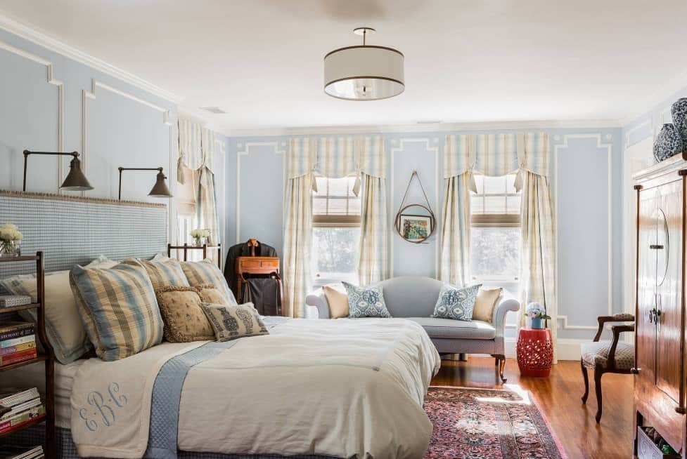 一间漂亮的主卧室，有漂亮的蓝色墙壁和可爱的窗帘，还有硬木地板，上面铺着漂亮的地毯。