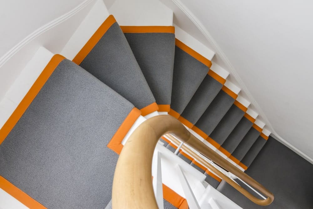 这个家拥有一个时尚的楼梯，灰色地毯地板，两边都有橙色的阴影。