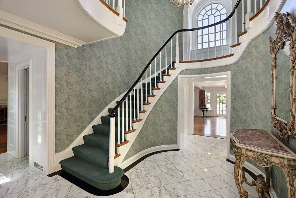 一个令人惊叹的楼梯，有优雅的墙壁和漂亮的绿色地毯地板，由一个华丽的吊灯悬挂在高高的天花板上。