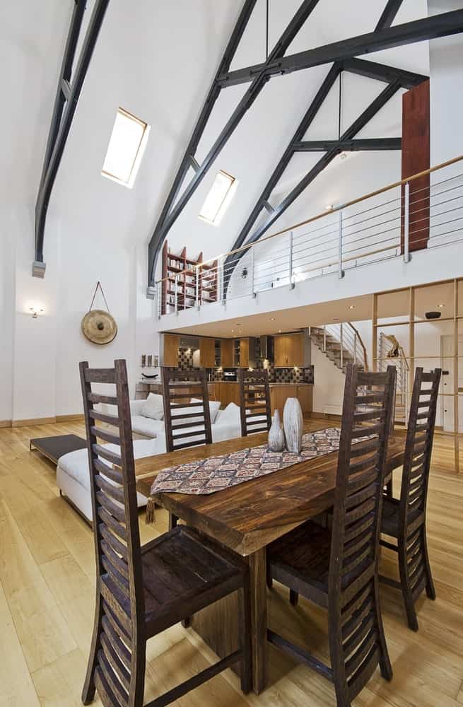 一个质朴的餐桌和一套时尚的高靠椅。该区域位于住宅的硬木地板上，在高高的天花板下。
