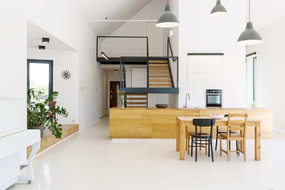 带厨房的现代住宅。它的特点是一个木制的柜台和一个木制的餐桌。房间以白色地板和高高的天花板为特色，由吊灯照明。