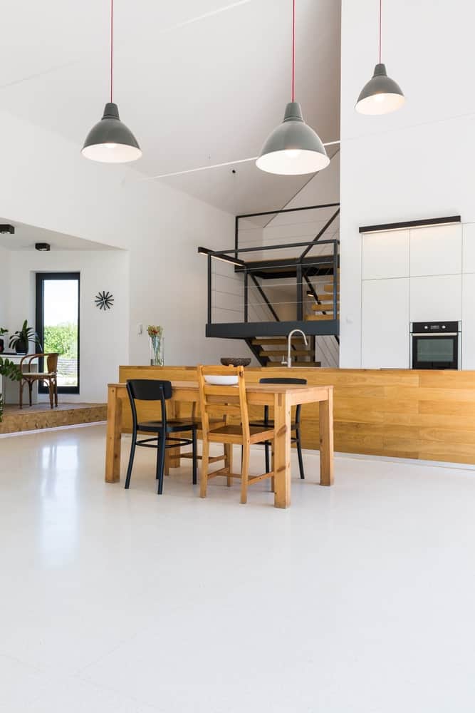 带厨房的现代住宅。它的特点是一个木制的柜台和一个木制的餐桌。房间以白色地板和高高的天花板为特色，由吊灯照明。