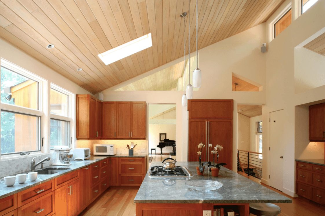 宽敞的厨房，有一个大的中心岛台，灰色大理石台面，由挂在带天窗的木棚天花板上的吊灯照亮。