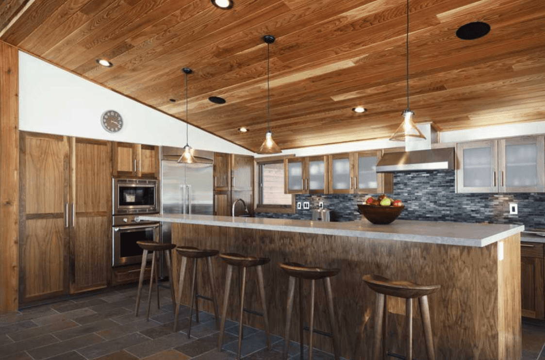 乡村风格的厨房有一个吸引人的中央岛，早餐吧台由木棚天花板上的吊坠灯泡照明。