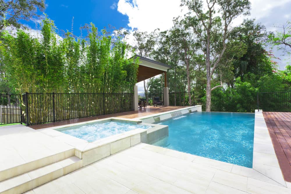一个带按摩浴缸的无边泳池和泳池边的小屋，周围环绕着宏伟的成熟树木。
