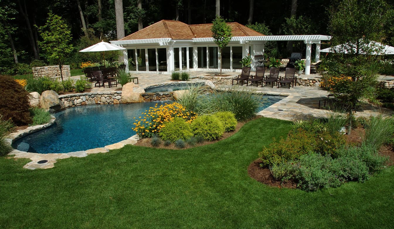 一个精心设置的游泳池，周围是郁郁葱葱的草坪，树木和植物。室外还提供多个休息区。