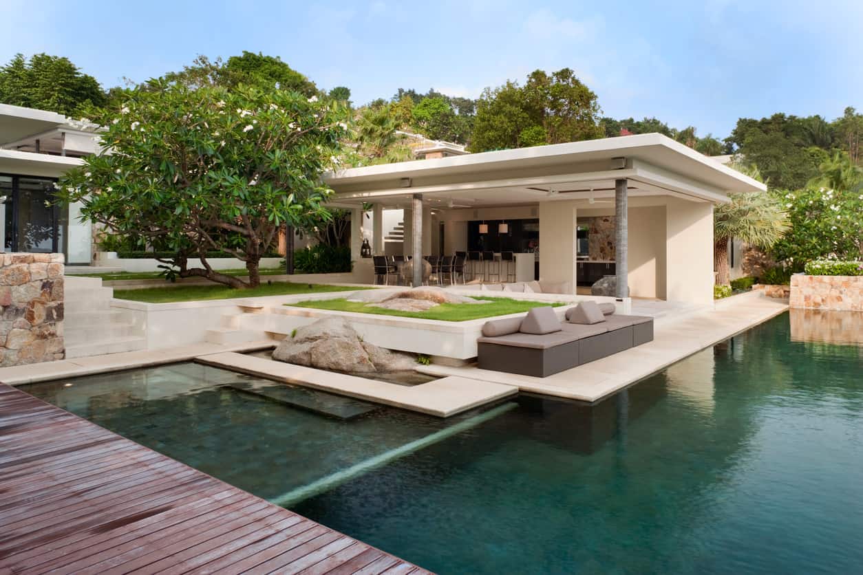 一个时髦的游泳池，有甲板和池边的房子，周围都是树木和植物。