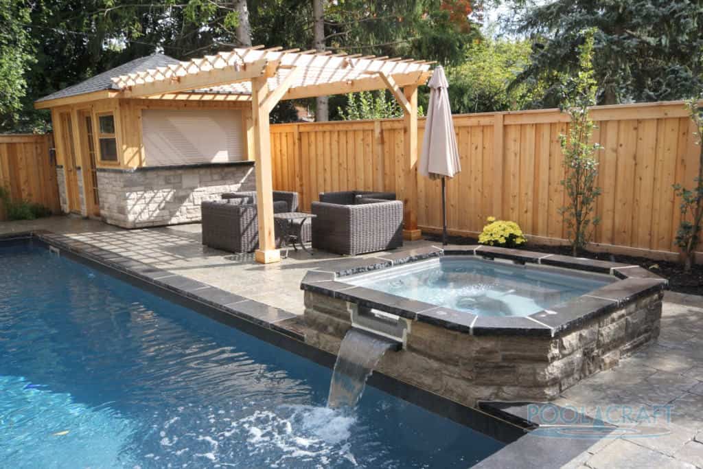 一个长方形的游泳池，设有按摩浴缸和泳池边的藤架，配有一套经典的藤条座椅。
