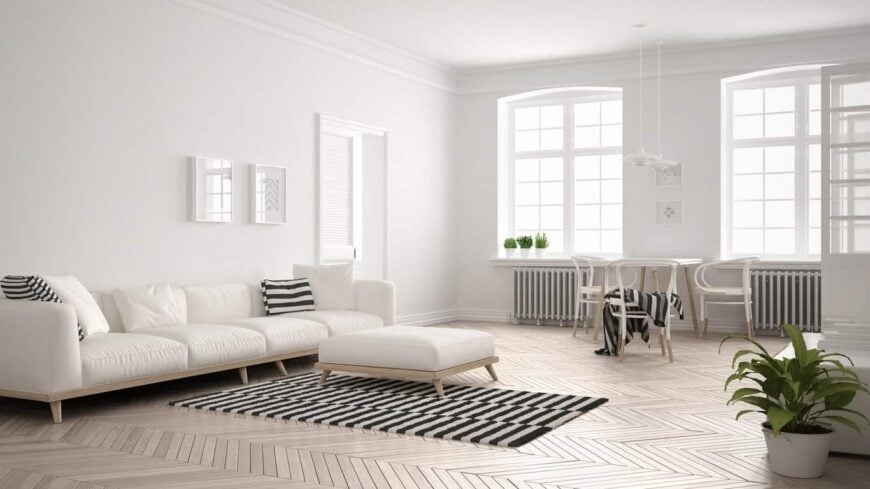 宽敞的斯堪的纳维亚风格的正式客厅以白色配色方案和人字纹硬木地板为特色。区域地毯、靠垫和毯子上的黑白图案，以及一些绿色的室内植物，是房间里唯一的色彩浮雕。