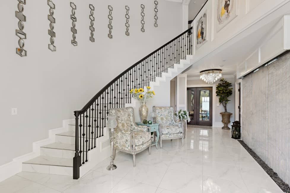 一个家庭入口设有优雅的大理石瓷砖地板，一对优雅的椅子和带有浓缩咖啡栏杆的楼梯。