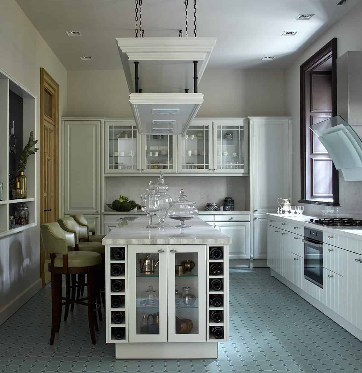 柔和的绿色瓷砖地板为厨房岛和半岛的白色橱柜提供了一个很好的背景，厨房岛和半岛有白色的摇瓶柜和抽屉。