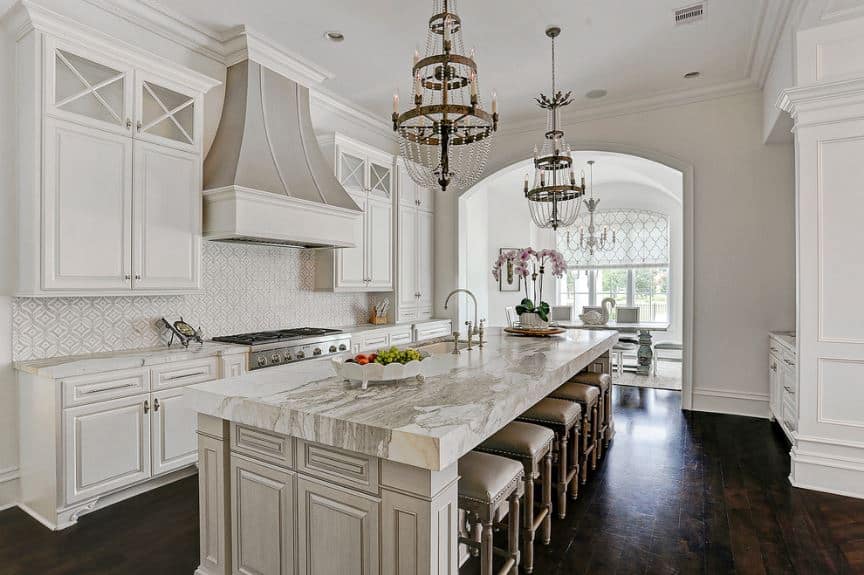 优雅的两层枝形吊灯悬挂在厨房岛台的白色大理石台面上，是这个配有深色硬木地板的厨房的突出元素。这与白色的橱柜、墙壁和天花板形成对比。
