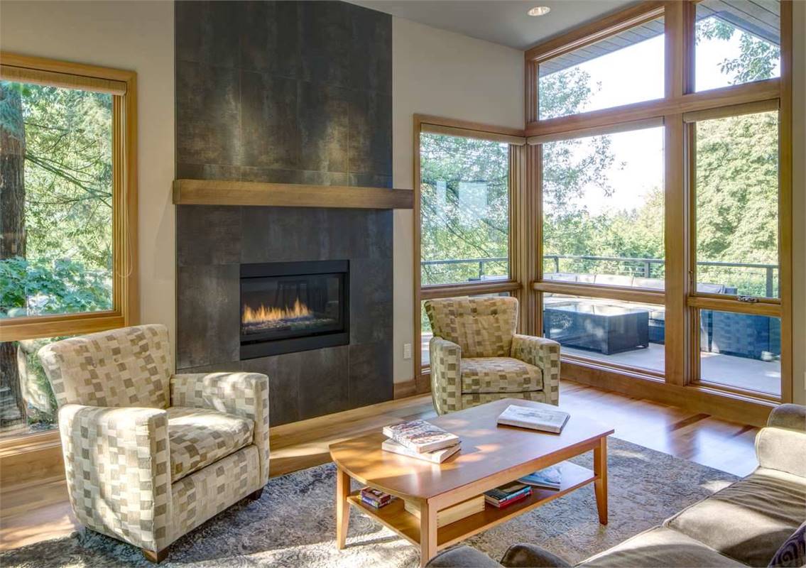 这间客厅设有现代化的壁炉，并配有图案扶手椅。屋内的自然光透过木质框架窗户照射进来。